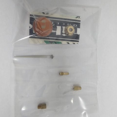 Clear plastic bag containing brass fittings and an orange plastic disc, with a long thin metal rod beside it.