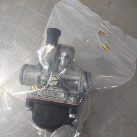 Metal automotive valve with multiple ports and a black cap, packaged in a clear plastic bag with small brass adapters