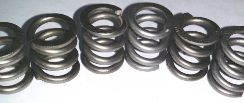 Row of metal compression springs arranged in a line on a light surface.