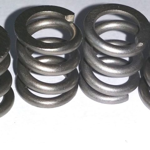 Row of dark metal coil springs laid in a line on a light surface, showing helical compression springs with visible ends.