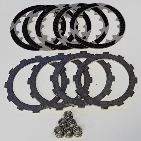 Assorted circular clutch plates (friction and steel) stacked with springs below on a white surface.
