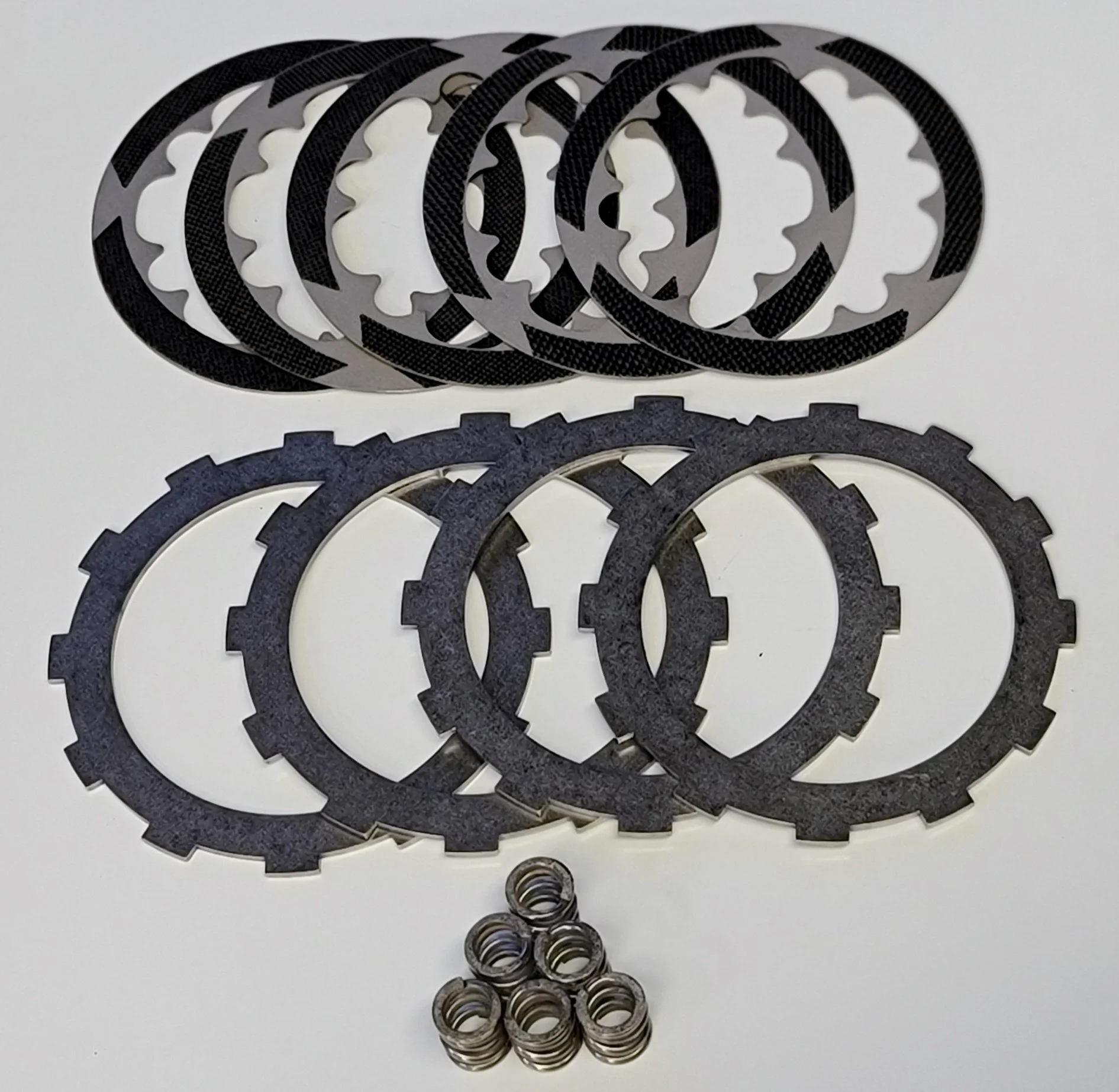 KTM-50cc-Stock-Friction-Kit - Inmotion Suspension Assorted circular clutch plates (friction and steel) stacked with springs below on a white surface.