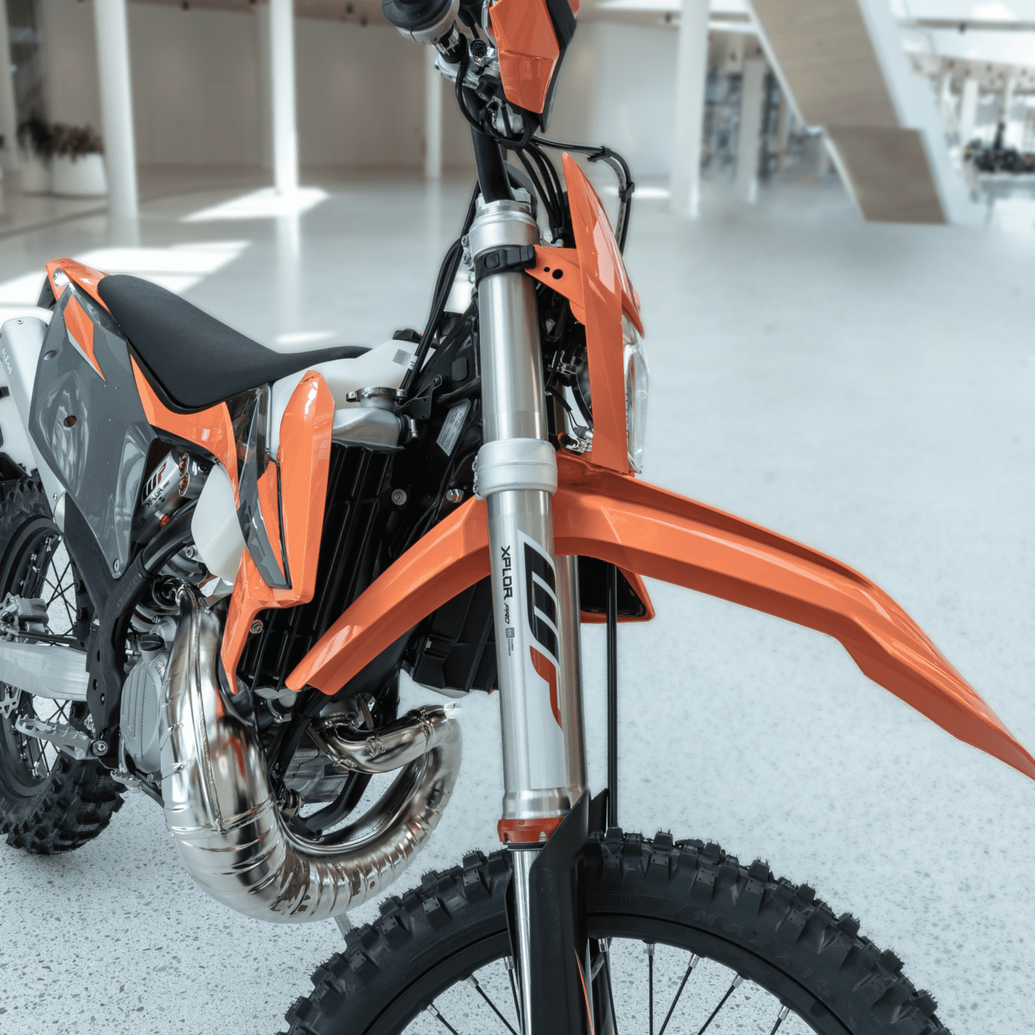 XPLOR PR04 - Inmotion Suspension Close-up of an orange off-road motorcycle front end in a bright showroom, showing the front suspension and knobby tire