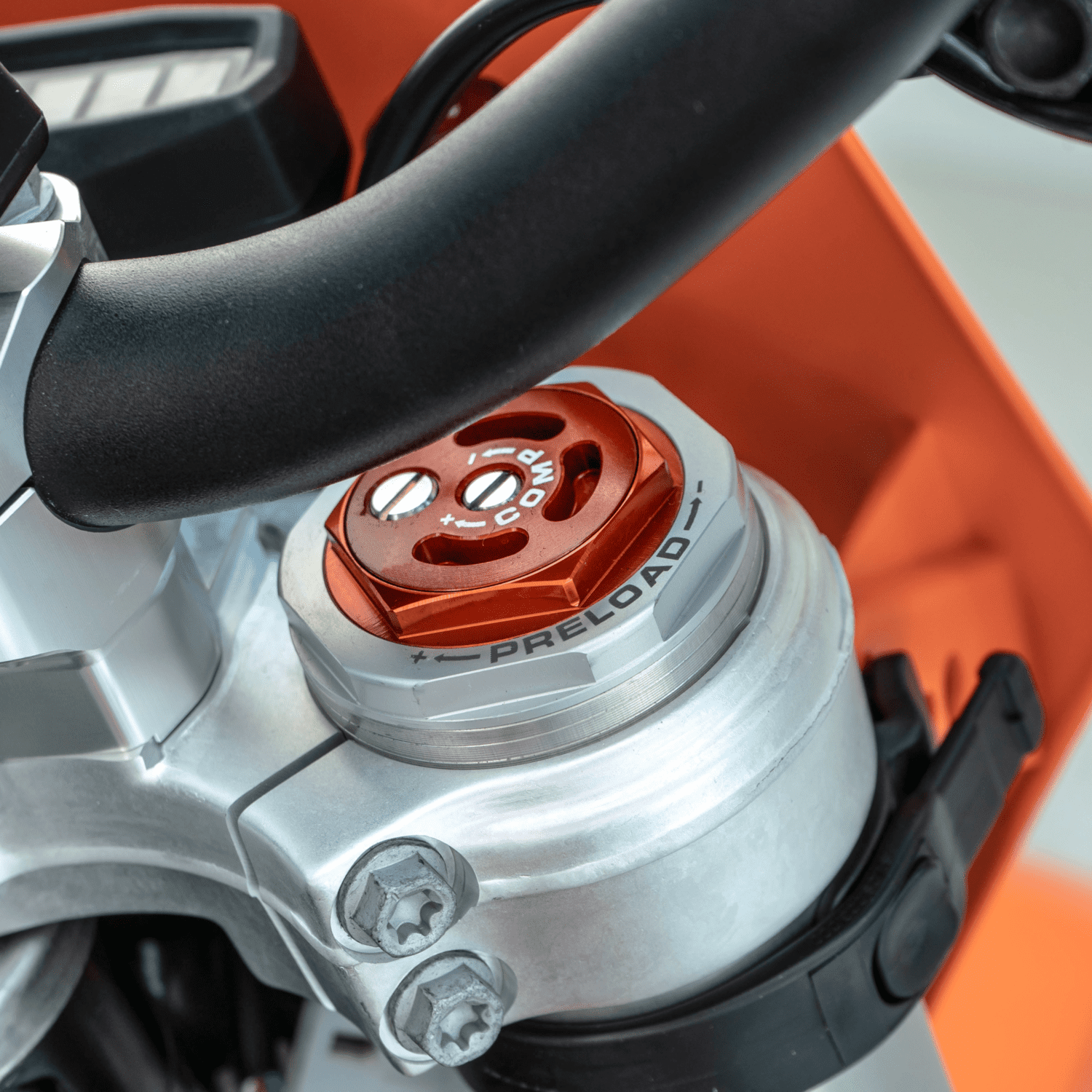 XPLOR Pro 3 - Inmotion Suspension Close-up of an orange motorcycle suspension preload dial with + and - signs and two screws nearby.
