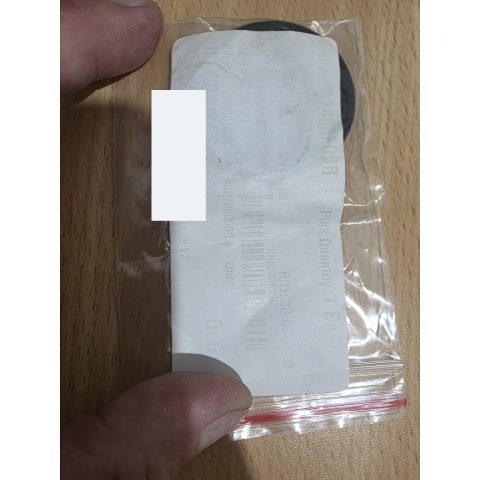 Close-up of a hand peeling a white label from a small plastic package that contains a circular black item underneath.