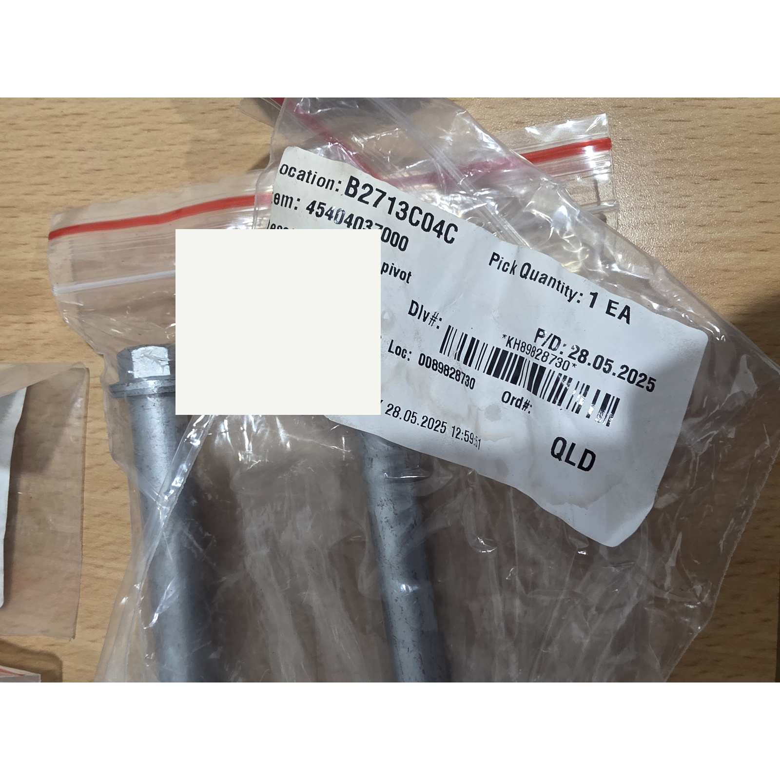 45404037000-a-cleaned - Inmotion Suspension Clear plastic zip bag containing metal rods on a wooden surface, with a white label showing location B2713C04C and pick quantity 1 EA.