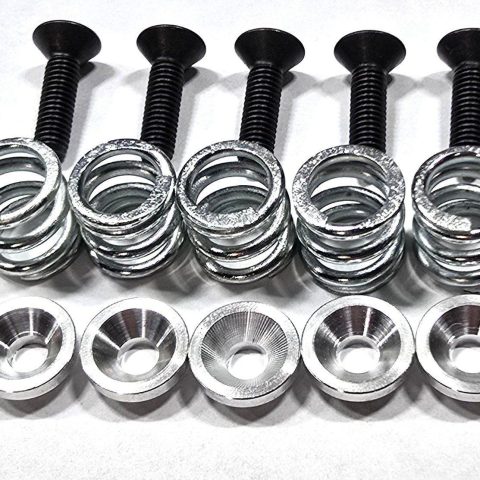 Five black bolts with threaded shafts, arranged above five silver washers on a light surface.