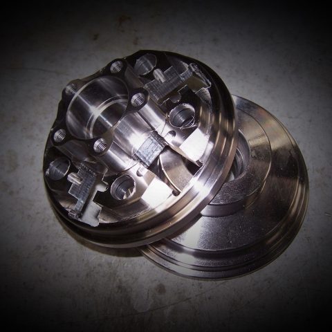 Close-up of a shiny metallic mechanical hub with bolt holes and interlocking parts on a dark vignette background.